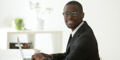 African-american,Smiling,Businessman,In,Suit,And,Glasses,Working,On,Laptop,